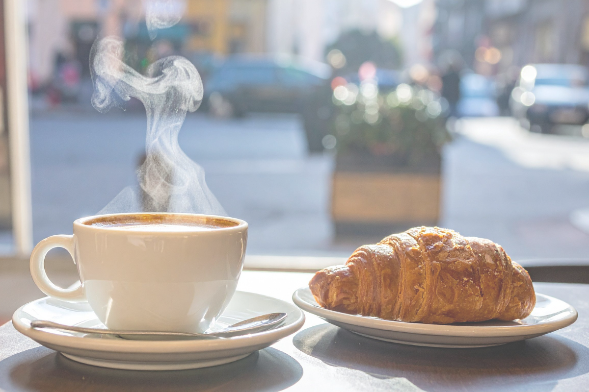 A latte and croissant on a table by a cafe window