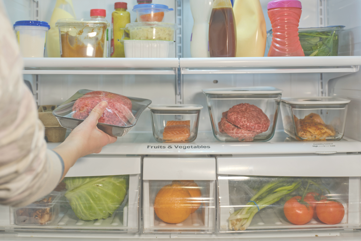 A person holding packaged food while looking inside a refrigerator