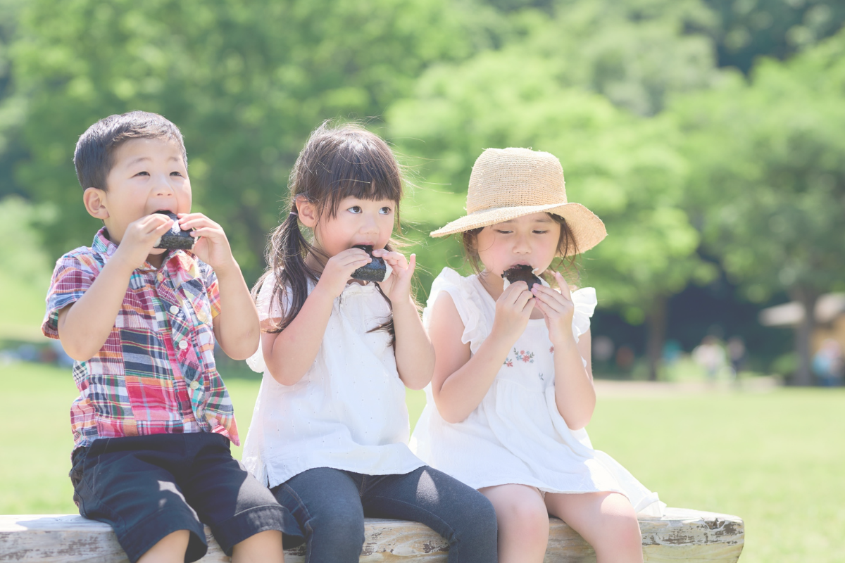 Three children eating food together outdoors